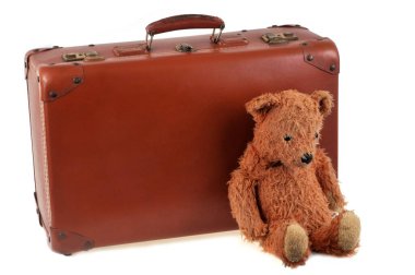 Oyuncak ayı, beyaz arka planda eski bir bavulun yanında.