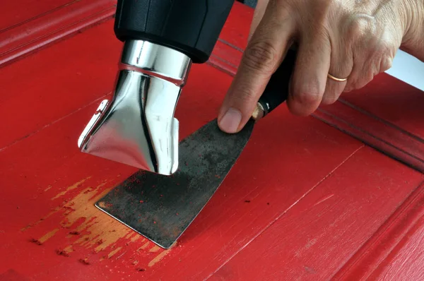 Removing red paint from furniture with a spatula and a heat gun in close-up