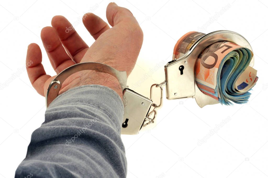 Concept of tax fraud with a hand cuffed to a wad of baqnue banknotes in close-up on a white background 
