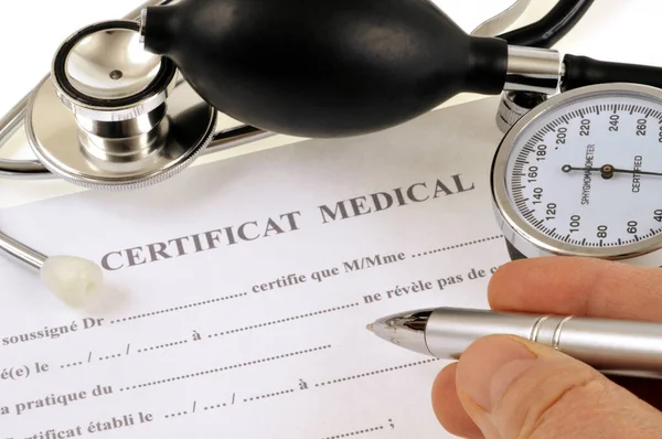 Completing a medical certificate with a pen next to a stethoscope and a blood pressure monitor close-up