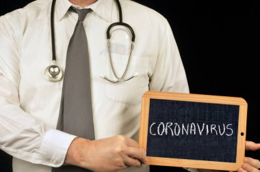 Üzerinde koronavirüs yazan bir okul tahtası tutan doktor. 