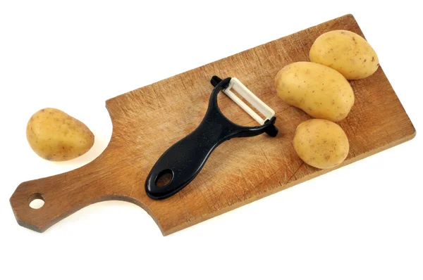 Patate Crude Tagliere Con Pelapatate Vicino Sfondo Bianco — Foto Stock