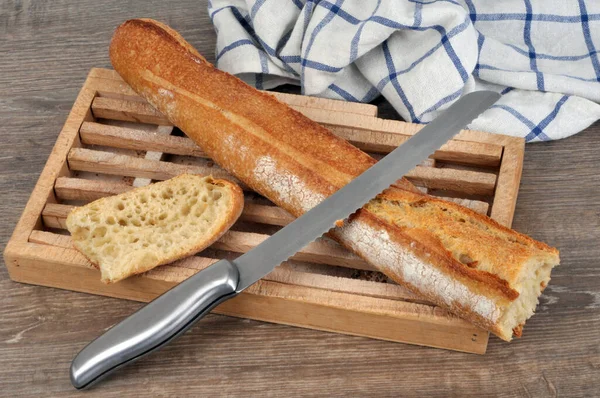 French traditional bread baguette on a bread board with a knife on gray background
