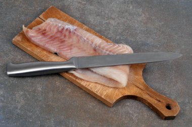 Kesme tahtasında bıçakla çiğ balık filetosu.