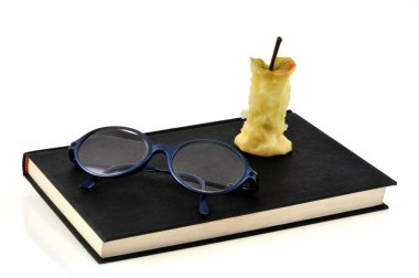 Gözlüklü bir kitap ve beyaz arka planda bir elma çekirdeği.