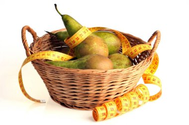 Beyaz arka planda bir metre terzi olan bir sepet armut.