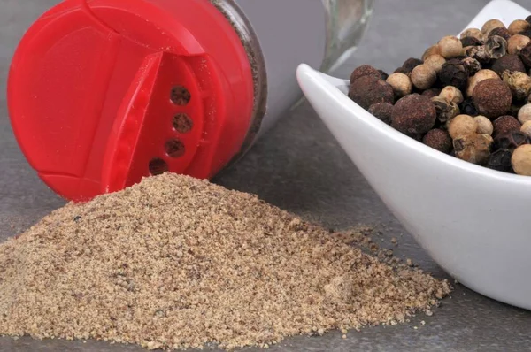 Bottle of spilled white pepper and ramekin of peppercorns close-up on gray background