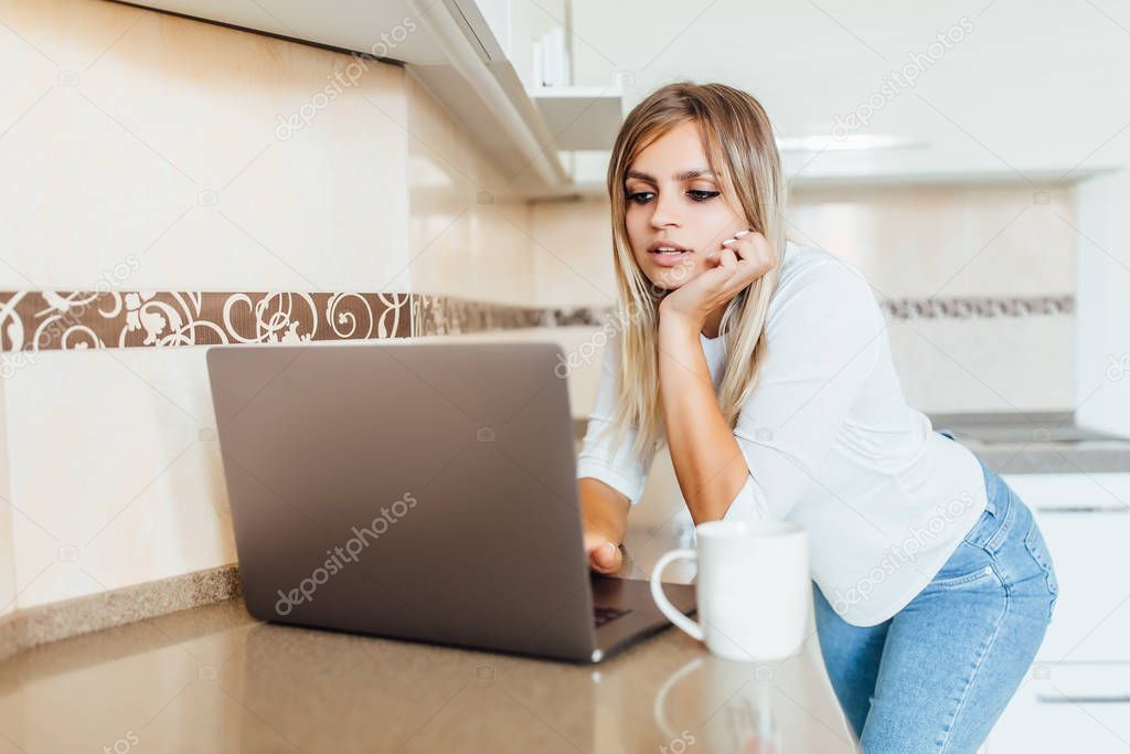 woman standing at table with buns in kitchen and looking at laptop, selective focus