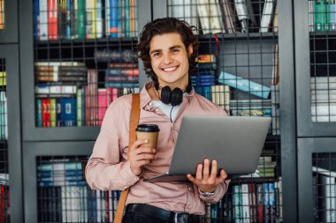Kahve molası sırasında üniversite kütüphanesinde oturan neşeli genç öğrenci.  