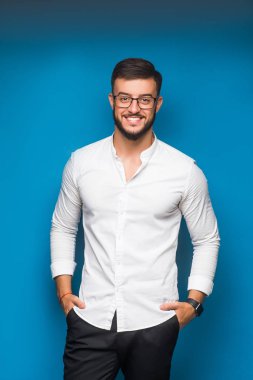 Beyaz gömlekli, mavi arka planda poz veren genç, yakışıklı serbest çalışan.