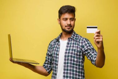 Mavi gömlekli Hintli adam kredi kartıyla online alışveriş yapmak için laptop kullanıyor.