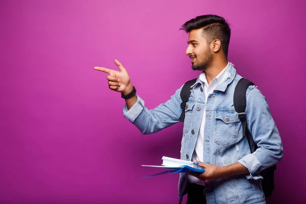 Handsome young indian student man reading notebooks while standing on violet background