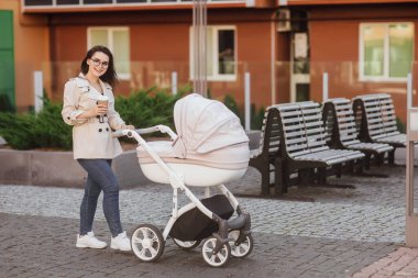 Kadın bebek arabası ve kahveyle yürüyor. Moda kızı, bebek arabalı anne. Anne ve çocuk..