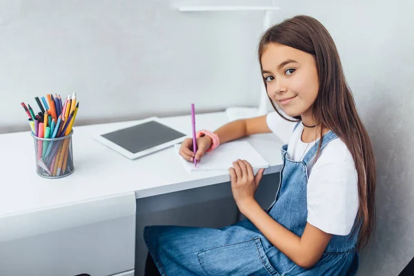 Menina Bonito Com Tablet Branco Fazer Anotações Enquanto Sentado Mesa — Fotografia de Stock