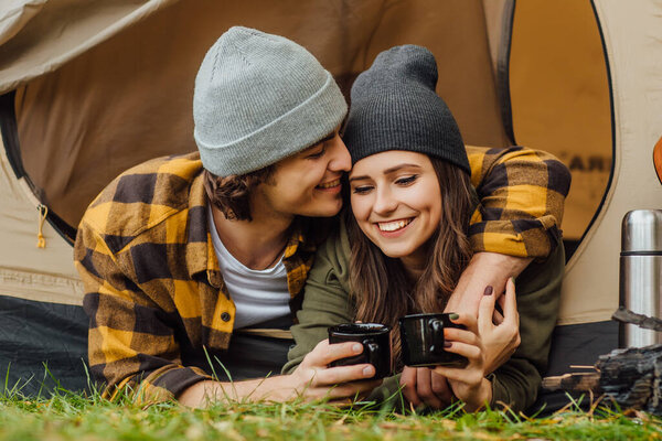 Portrait of young loved couple of tourists have a date in the forest. Attractive young woman and handsome man kissing in the tent.