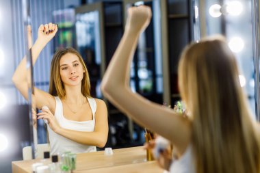 Aynanın önündeki güzel kız vücut hijyenini korumak için deodorant sürüyor..