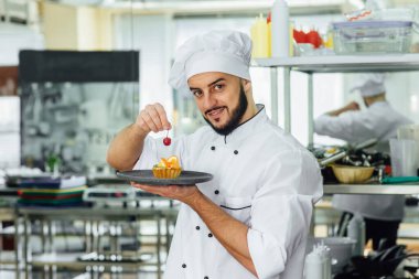Restoranın mutfağındaki genç, sakallı ve yakışıklı şefin portresi hazır meyveli tatlı bir pastayla.