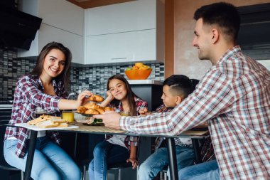 Genç ve mutlu bir aile mutfakta ayçöreğiyle kahvaltı yapıyor, annesi ellerinde tatlı ellerle. Aile zamanı..