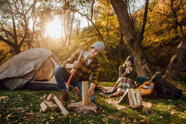 Genç turistler birlikte yeni yerler keşfediyorlar. Çekici kadın çay içip kütüğün üzerinde otururken baltayla odun kesen yakışıklı bir adam gibi görünüyor..