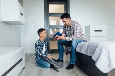 Baba, sabah evde kitap okurken oğlunun okula hazırlanmasına yardım et..