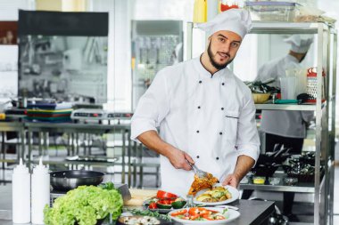 Neşeli şef, restoranın mutfağında otlu patates ve beyaz tabakta balık servis ediyor, yakın plan. Aşçı tabağa domates sosu döker..