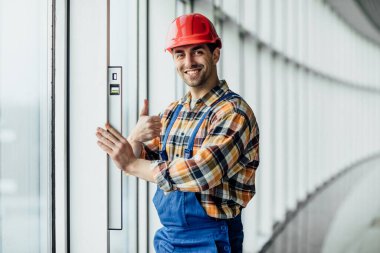 İnşaat işçisi ve tamirci ofis tadilatı üzerinde çalışıyor. İnşaatçı, dengeleyici araç kullanarak duvar odasını ölçüyor ve kontrol ediyor.