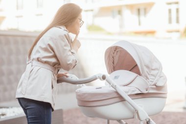 İlgilenen genç anne bebek arabasında kalıyor ve ağlayan bebeği sakinleştiriyor. Aile kavramı.