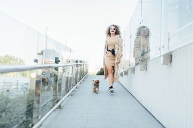 Parkta köpeğini gezdiren, sıradan kıyafetler giyen genç bir moda kadını portresi..