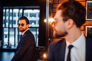 Model portresi ya da sakallı yakışıklı iş adamı aynanın yanında durup poz verir..