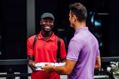 Kuryeden pizza kutusunu alan gülümseyen bir çalışan, Afro-Amerikan genç adam, şirket öğle yemeği molasında yemek servisi sipariş etti. .