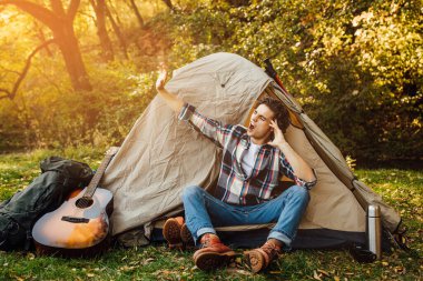 Genç yakışıklı adam, sabahları esniyor ve esniyor. Kamp alanında çadırın yanında..