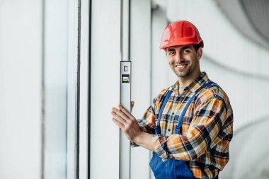 Miğferli ve tamirci, ofisin yenilenmesi üzerinde çalışıyor. İnşaatçı, dengeleyici araç kullanarak duvar odasını ölçüyor ve kontrol ediyor.