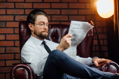 Yakışıklı, stil sahibi, mavi takımlı bir milyoner. Kanepede oturuyor ve taze gazete okuyor..