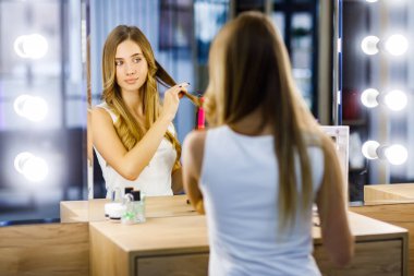 Sarışın kız, aynanın önündeki saç maşasıyla kafasında bukleler yapıyor..