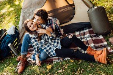 Genç bir çift ormanda kamp yapıyor ve eğleniyor. Güzel bir kadın ve yakışıklı bir erkek battaniyenin üzerinde çadırın yanında oturarak doğada vakit geçiriyorlar..