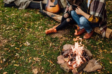 Kamp yaparken çadırın yanındaki insanların bacaklarının fotoğrafını çek. Ateşe odaklan. Bacaklar kamp ateşinin yanında. Genç bir çift turist, doğadaki şenlik ateşinin yanında dinleniyor..
