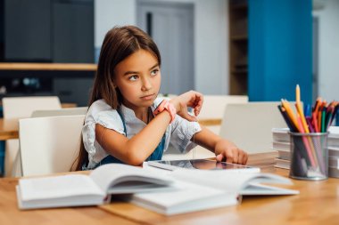 Masada oturan sevimli ve mutlu küçük kız, akıllı saatini kullan..