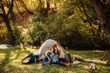 Genç çift ormanda kamp kuruyor. Güzel bir kadın ve yakışıklı bir adam kameraya bakıyor, çadırın yanında oturuyor..
