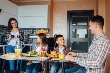 Mutfakta sütle kahvaltı yapan mutlu bir aile, kahveyle fincan tutan bir anne..