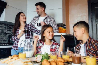 Aile mutfakta kahvaltı yapar, çocuklar birlikte otururken pasta yer..