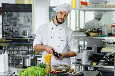 Profesyonel bir erkek aşçı profesyonel bir mutfakta eğleniyor, salata ve spagetti hazırlıyor..