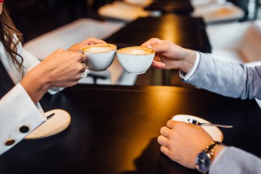 Kafedeki kahve fincanlarıyla kahve bardaklarını tokuşturan kadın ve erkeğin görüntüsünü kapatın..