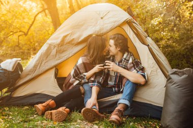 Çadırın yakınındaki bir kamp alanında rahat elbiseli genç ve güzel bir çift oturuyor. Çekici kadın ve yakışıklı erkek arkadaş eğleniyor, çay içiyor ve ekose kumaşın üzerinde oturuyor..