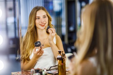 Güzel kız makyaj yaparken yüzüne pudra sürer..