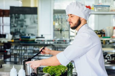 Beyaz cüppeli genç, yakışıklı bir adam makarna hazırlıyor, İtalyan spagettisi için su kaynatıyor..
