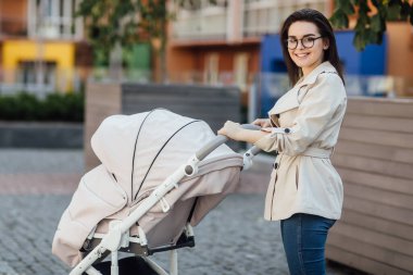 Pusetli güzel bir anne parkın yakınında yürüyor. Açık havada bir bebekle yürüyorum. Yeni doğan, aile, çocuk, ebeveynlik.