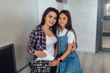 Anne kızının okul için hazırlanmasına yardım eder. Anne çocuğuna sırt çantası takması için destek oluyor..