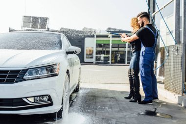 Araba yıkama, kadın çamurdan motoru temizlemek için sprey köpükle ayakta duruyor..