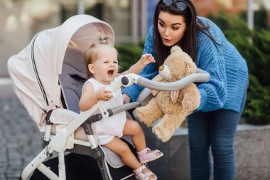 Anne bebek arabasıyla geziyor, kadın oyuncak ayıyı tutuyor ve bebeğiyle vakit geçiriyor..
