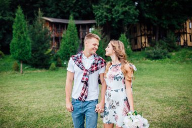 Genç, güzel, gülümseyen bir çift yaz parkında çiçeklerle tarlada yürüyor..